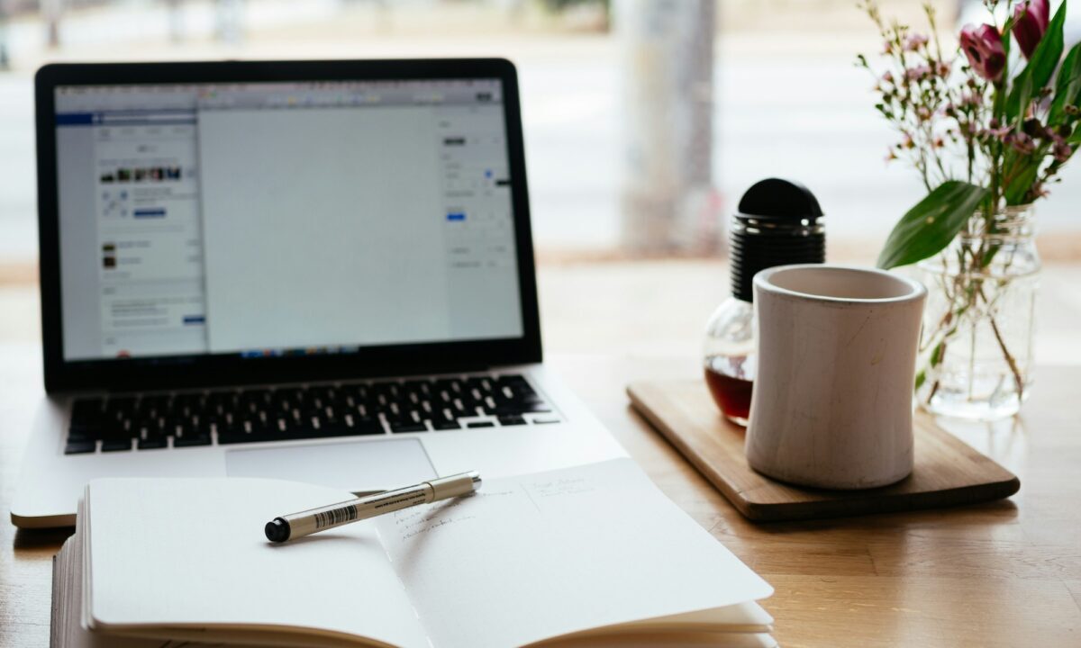 Notebook with marketing terminology written in it, with pen laid across it, sits on a desk in front of a laptop and cup of coffee